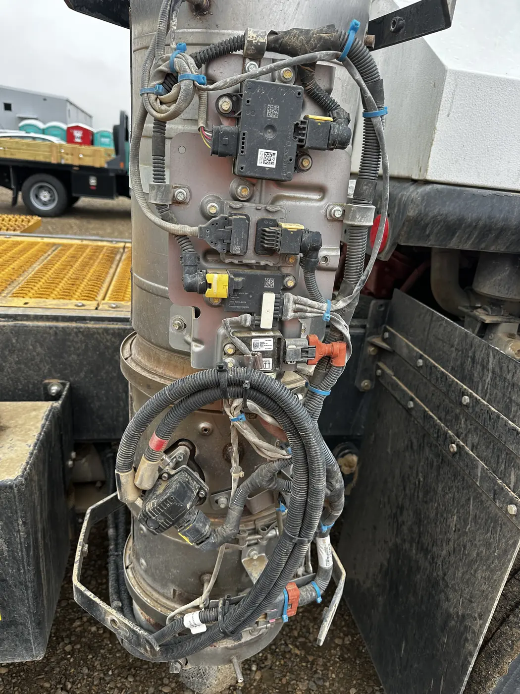 A vertical stainless aftertreatment canister mounted behind the cab with sensors, control modules and wiring attached