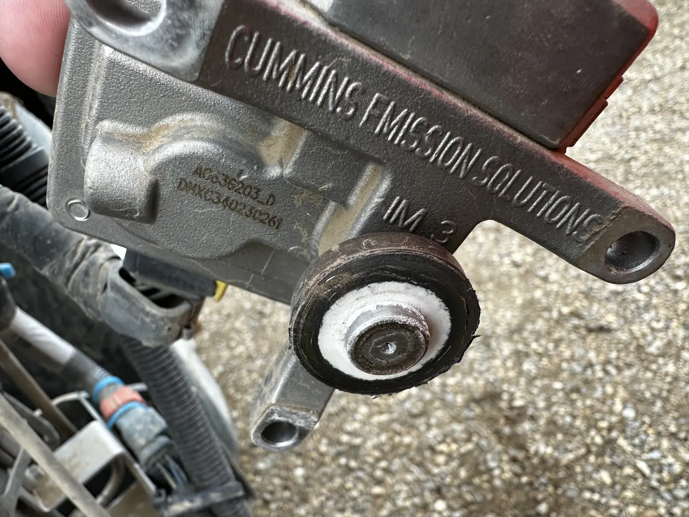 A DEF injector held in a technician's hand, cast Cummins Emission Solutions, with white crystalline buildup around the tip