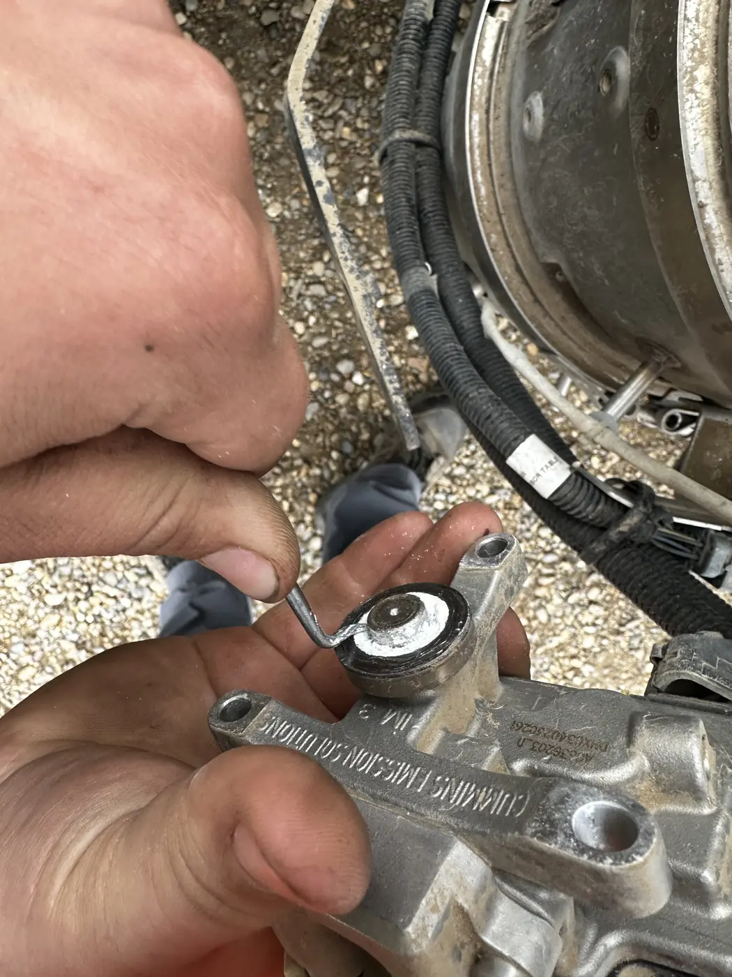 Two hands working a pick around the tip of the removed DEF injector over the open aftertreatment housing