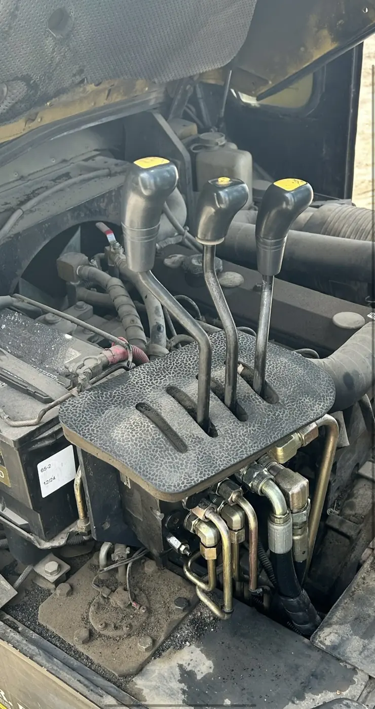 Forklift mast control levers and connected hydraulic lines beneath an opened cover