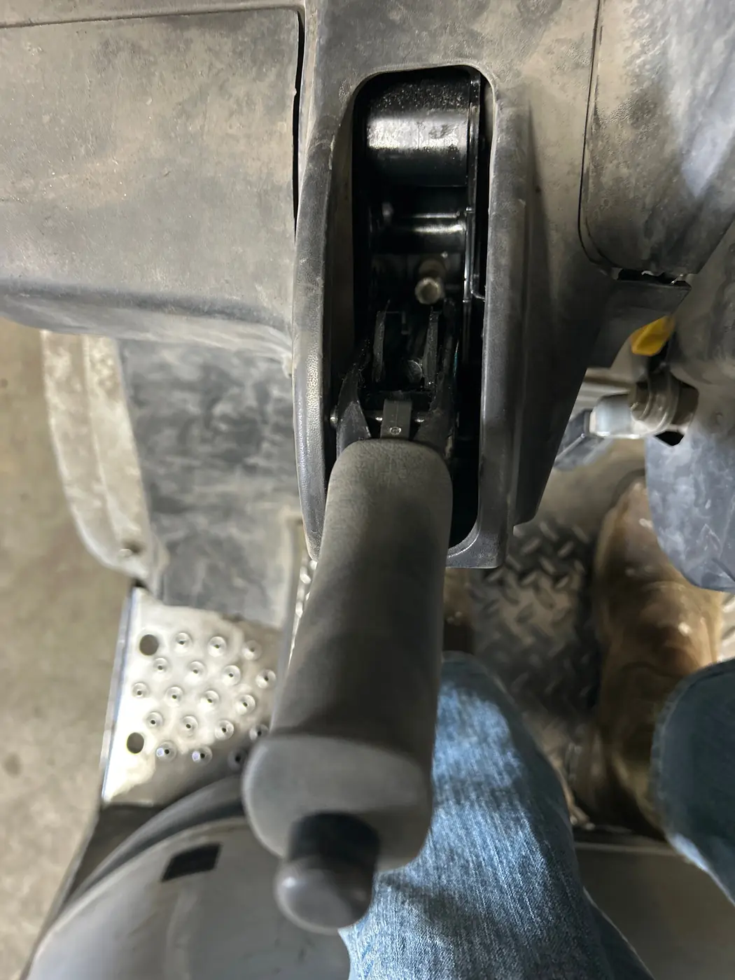 Parking brake lever with its linkage visible through an opening in the operator console