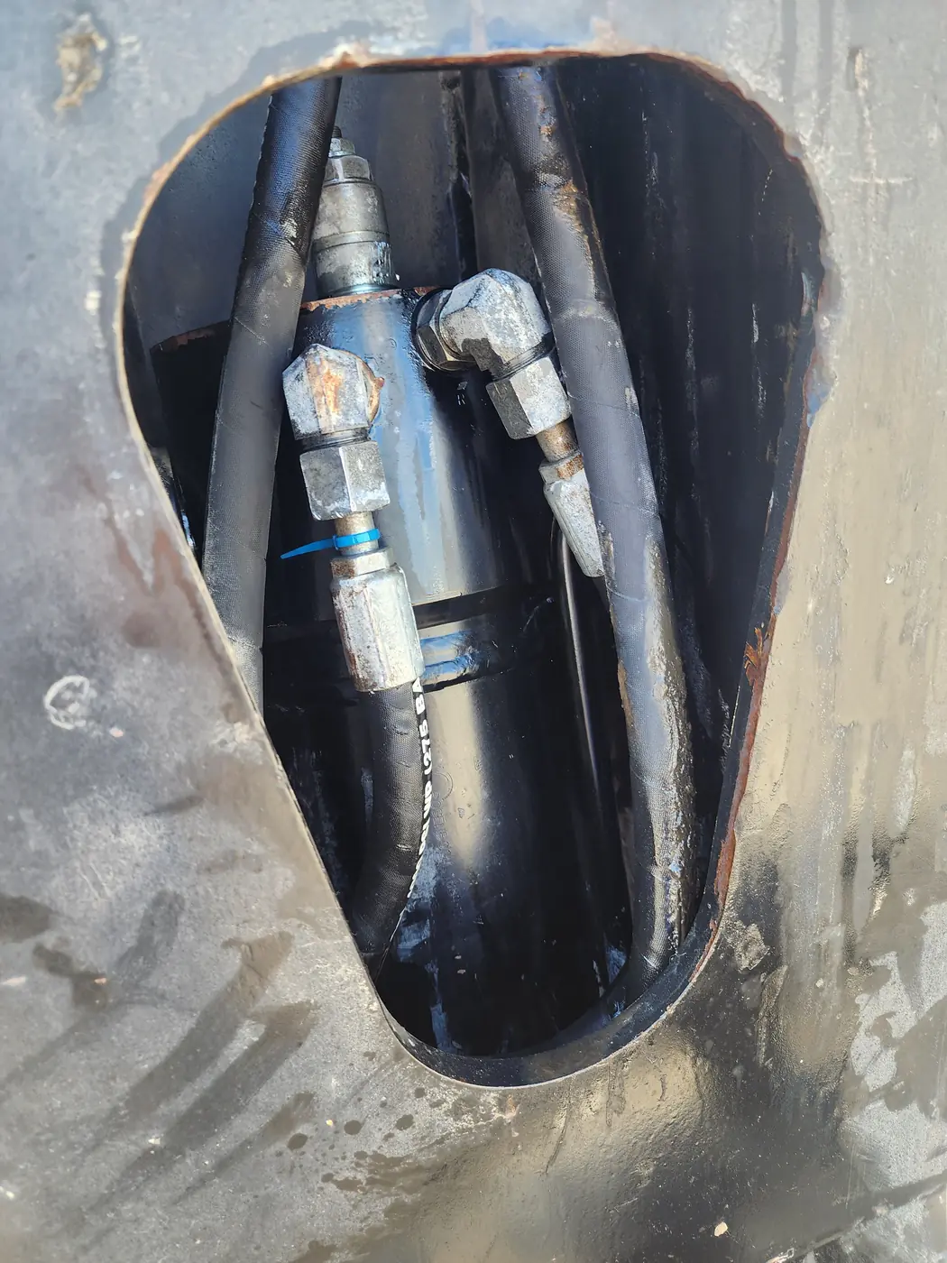 A hydraulic cylinder and its hose fittings seen through an access opening in the telehandler boom