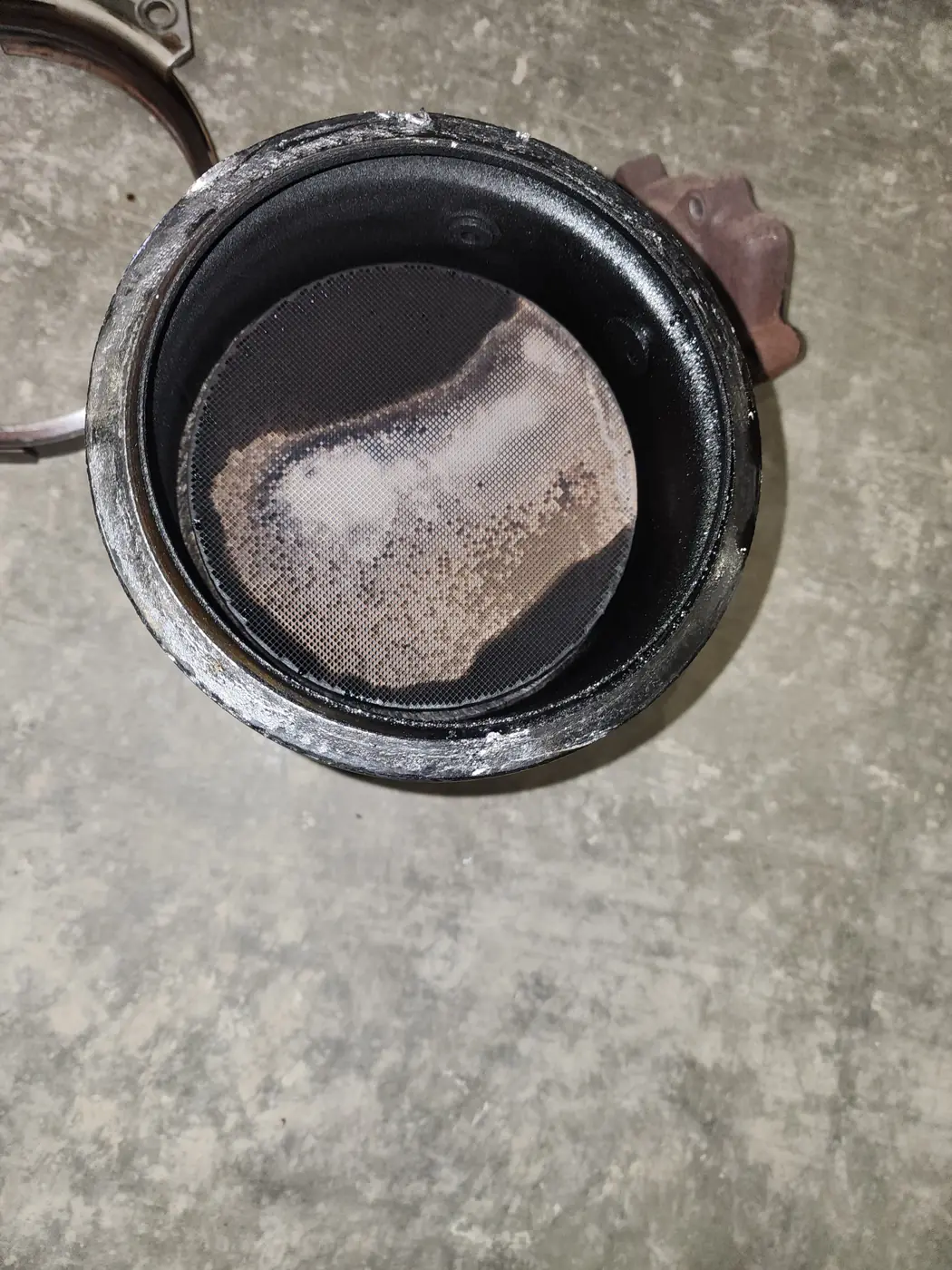Looking into the exhaust aftertreatment canister with its face loaded with soot and oil