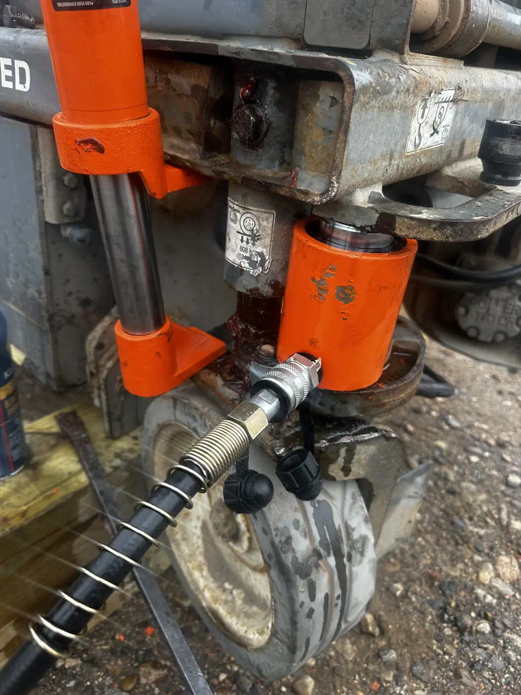Two hydraulic rams and a hose rigged against the machine frame at the steer wheel