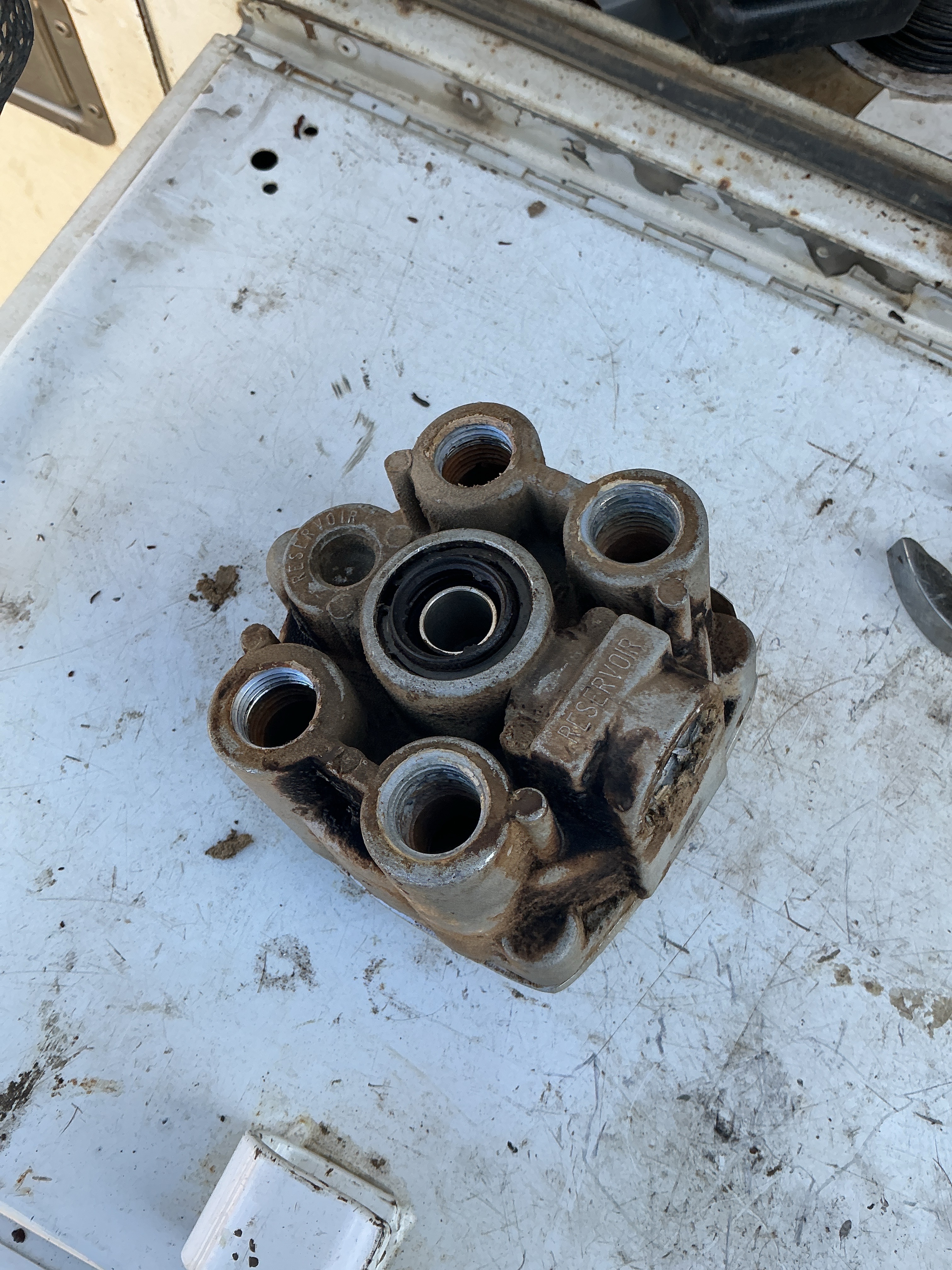 Removed relay-valve body with threaded air-line ports on a service work surface.