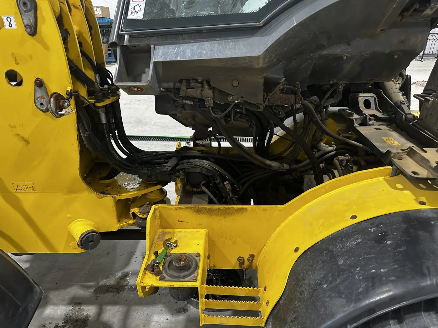 The wheel loader with its cab tilted up, exposing hydraulic hoses and hard lines underneath