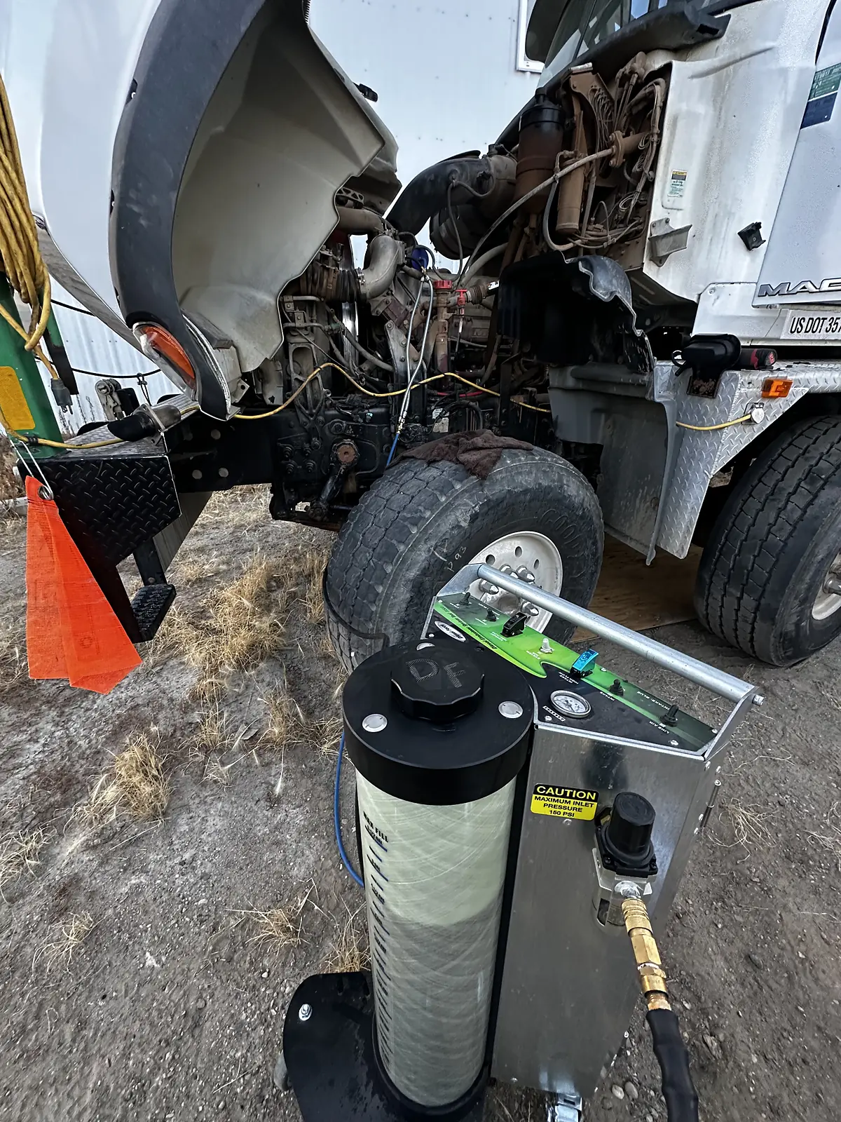 Portable filtration equipment connected beside the open engine bay of a white truck