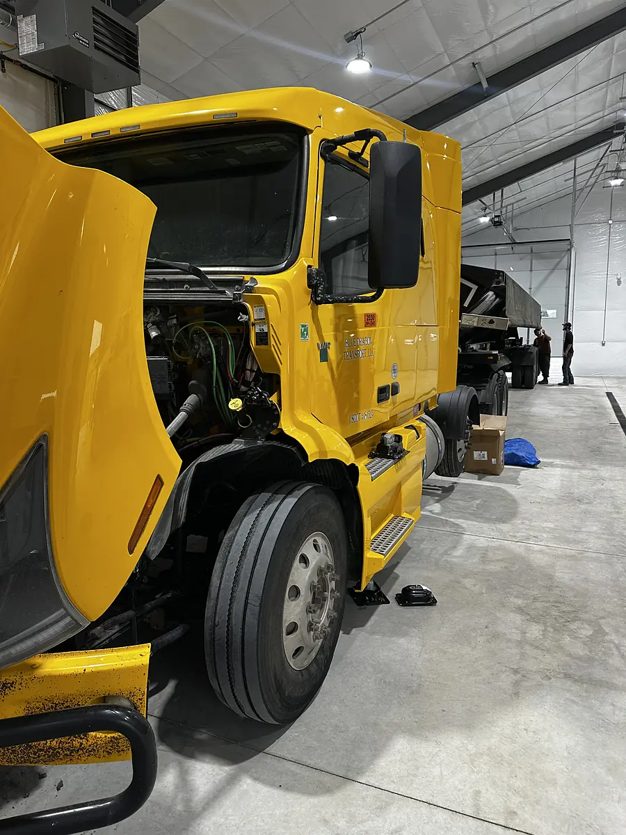 Yellow heavy truck with its hood open inside the repair shop