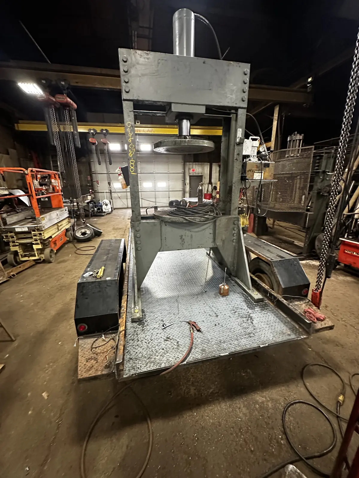 The tire press mounted on a two axle trailer, standing on a shop floor with its deck empty